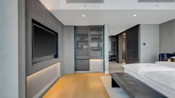 Un dormitorio moderno con una televisión grande, almacenamiento integrado, un banco y un vestidor.