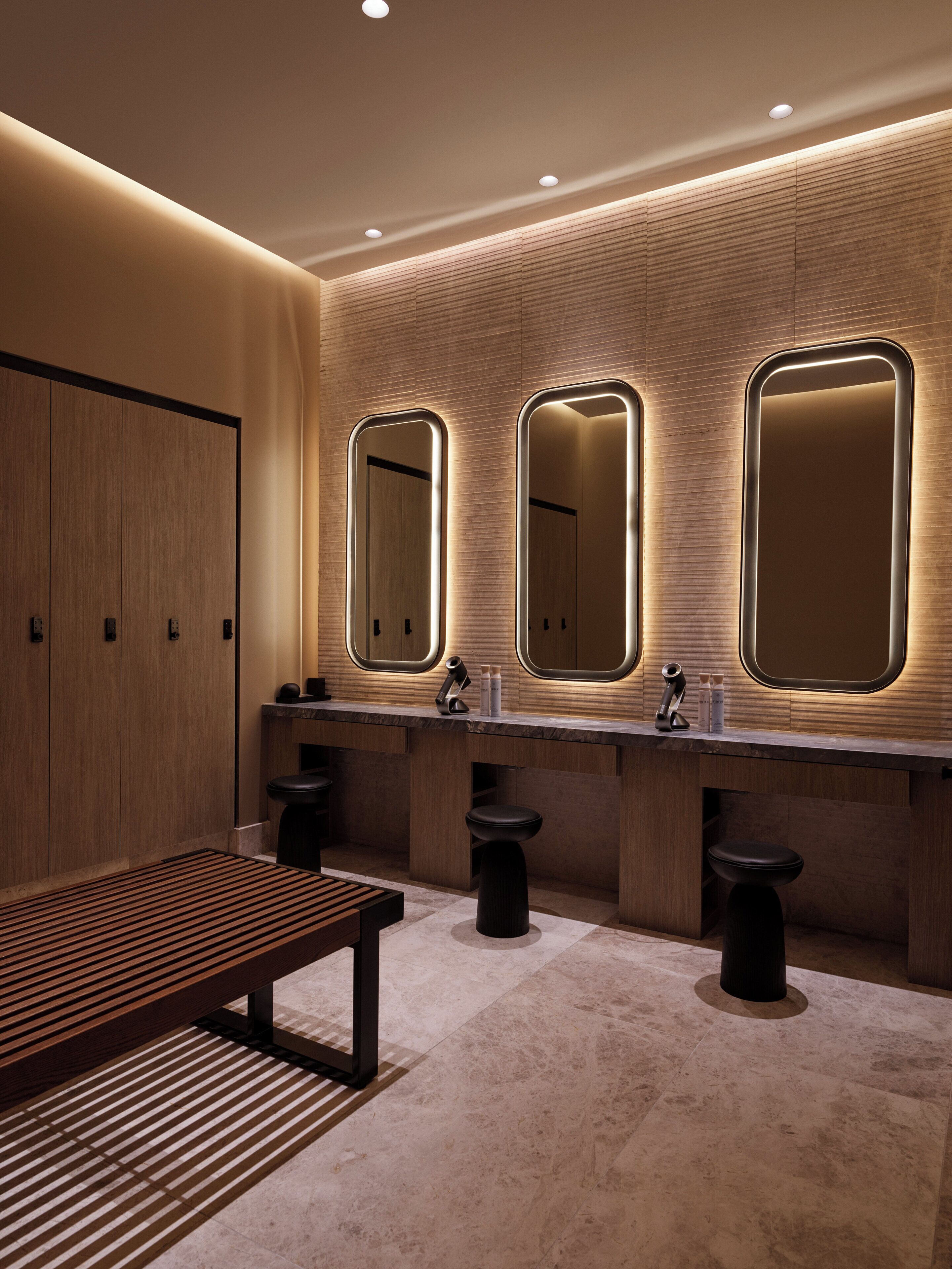 A modern restroom with three sinks, a bench, and a wooden wall.