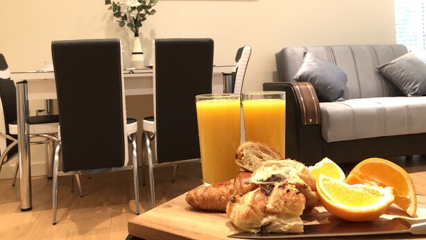 A dining table with breakfast items including croissants, orange slices, and a glass of orange juice. - Park View 2 Bedroom By Creatick (Maidenhead)