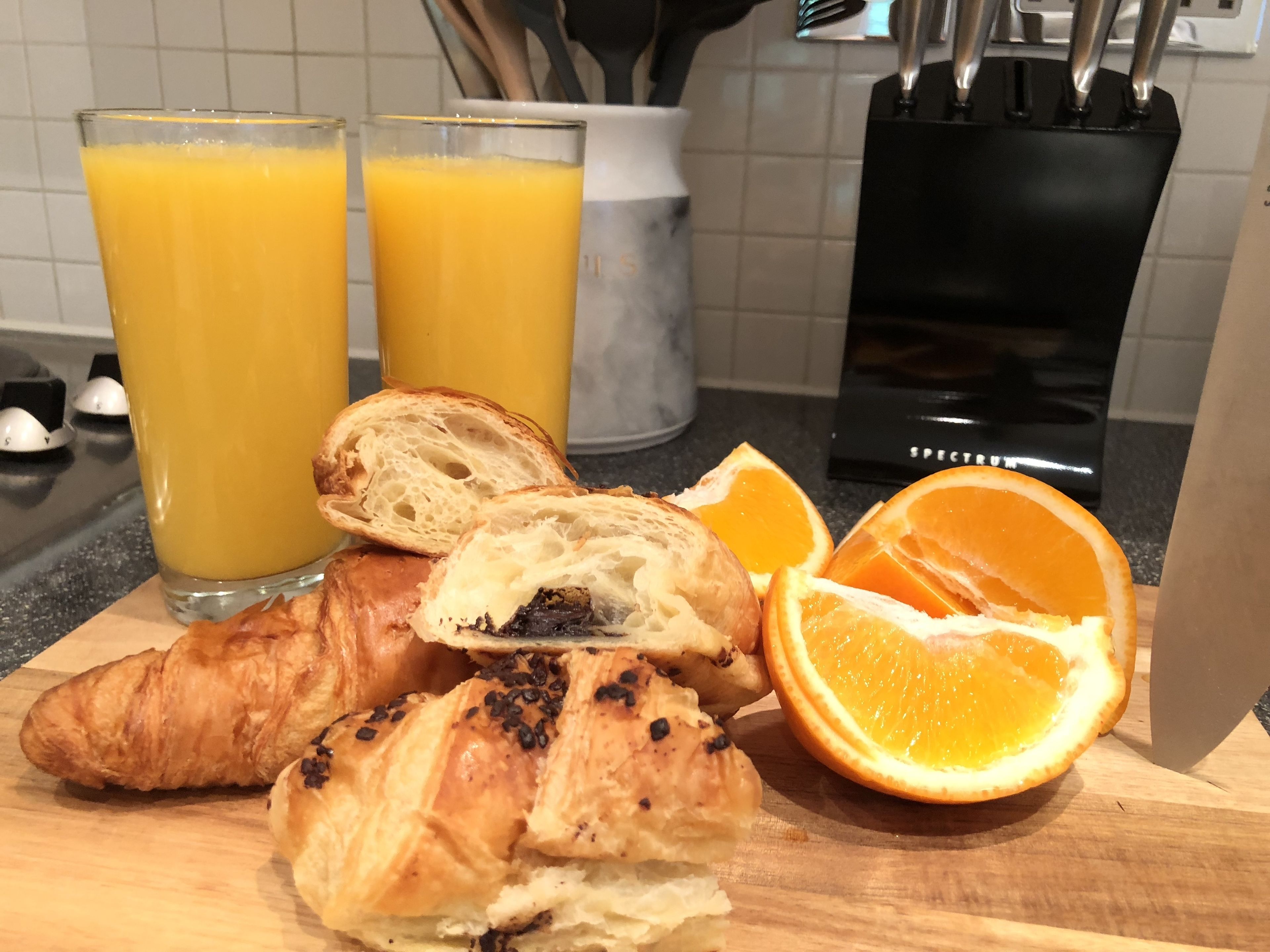 Desayuno con croissants, zumo de naranja y una rodaja de naranja sobre una tabla de madera.