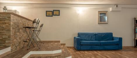 Una sala de estar con un sofá azul, una escalera y una pequeña mesa con sillas.