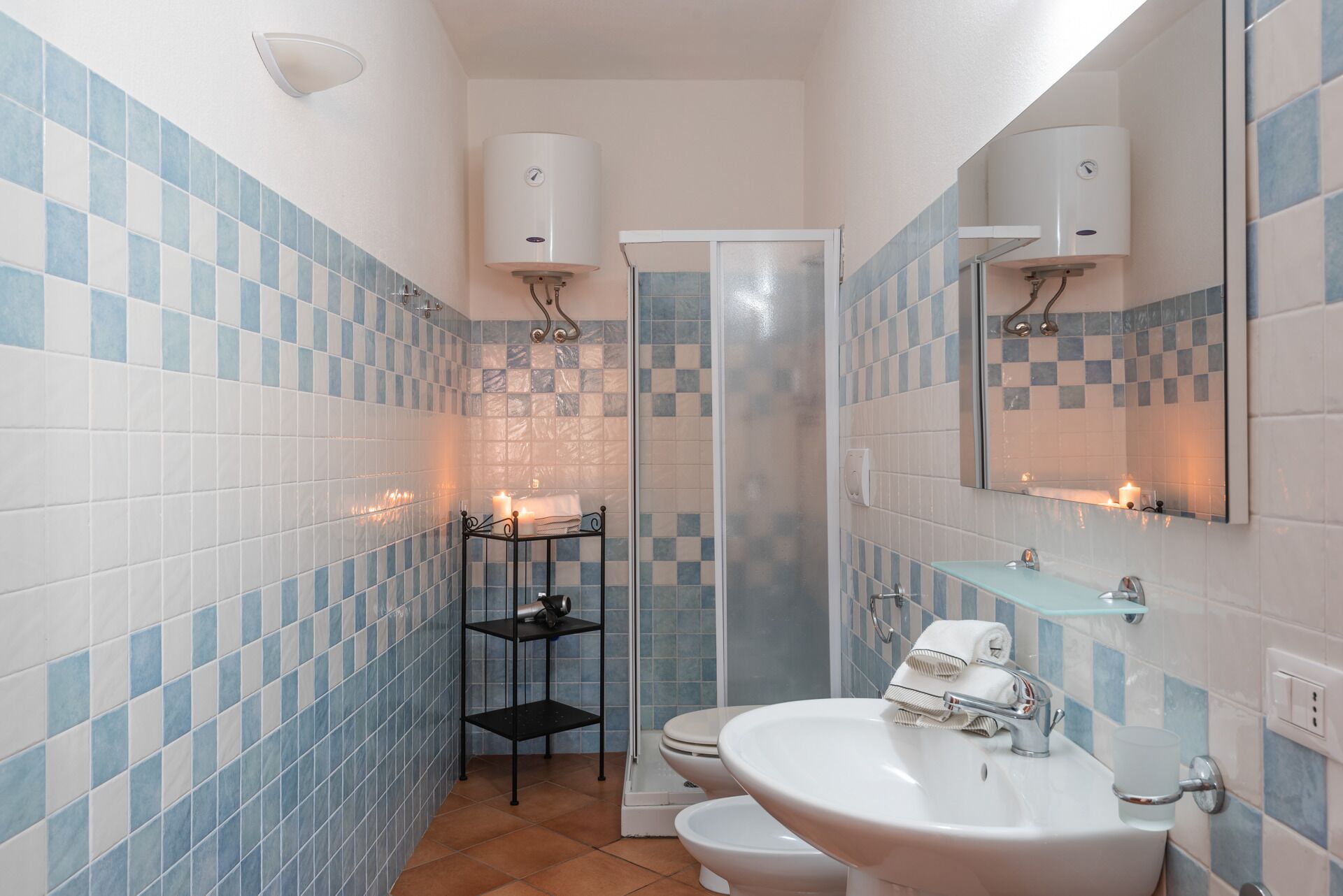 A bathroom with blue and white tiles, a white sink, two toilets, a glass shower enclosure, and a mirror with a towel rack.