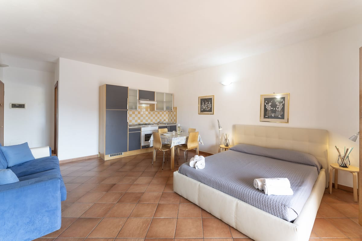 Habitación de hotel con cama, sofá, zona de comedor y kitchenette.