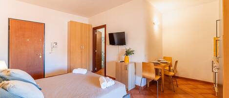 Une chambre d’hôtel avec un lit, un bureau, une chaise, une télévision et une petite table sur laquelle se trouve un vase.