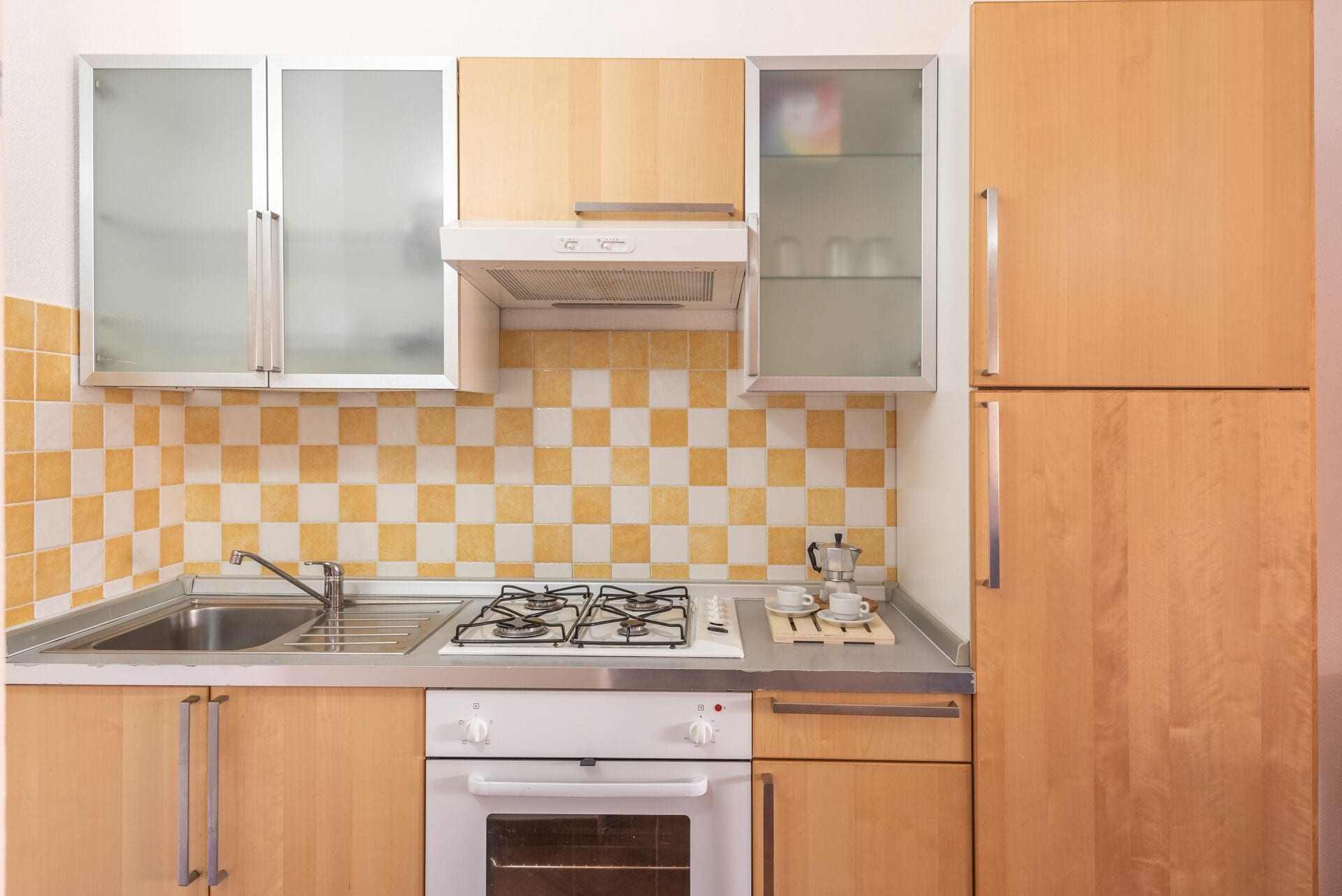 Een keuken met een gasfornuis, oven, spoelbak en houten keukenkastjes.