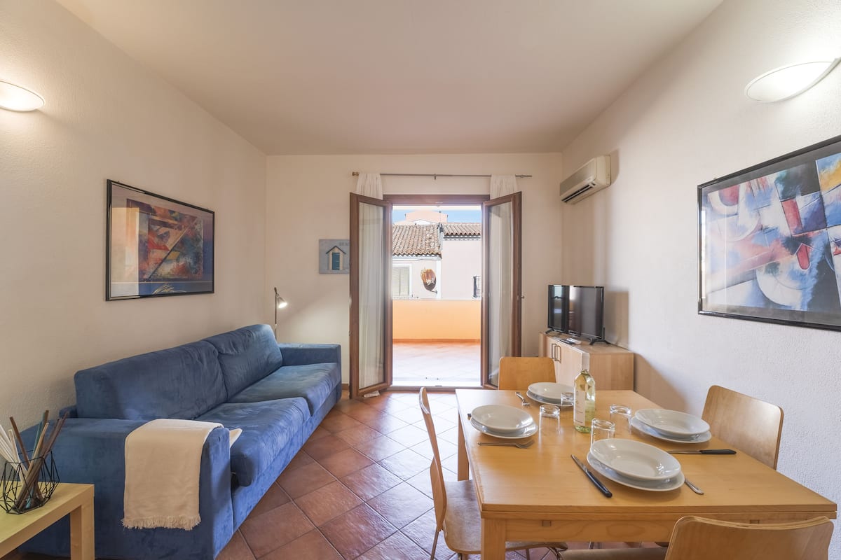 Una sala de estar con un sofá azul, una mesa de comedor con platos y cubiertos, y un televisor sobre un mueble de madera.