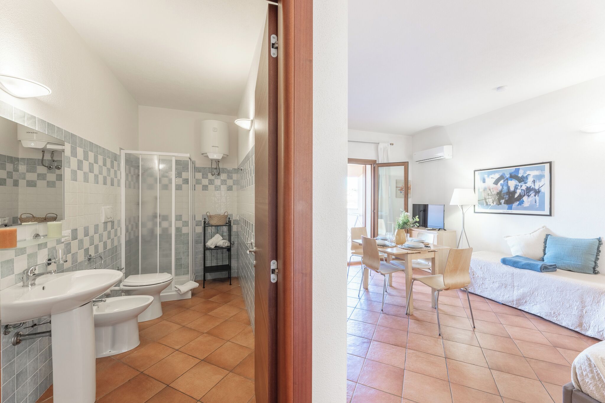 Un baño moderno con ducha, inodoro y lavamanos. Hay un comedor con mesa y sillas, y una sala de estar con sofá y un cuadro en la pared.