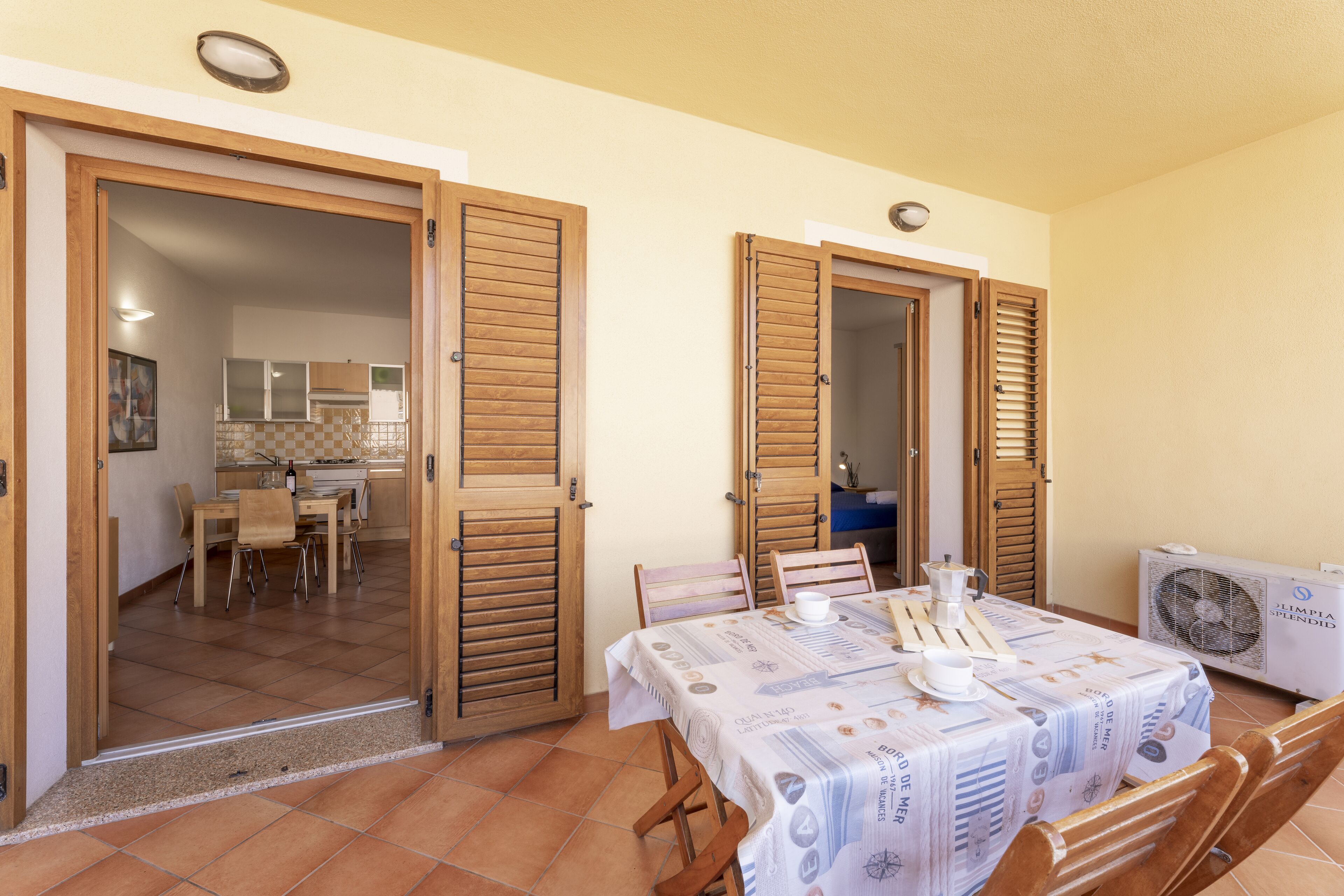 Comedor con una mesa dispuesta para dos, puertas de madera y una cocina visible a través de un vano abierto.