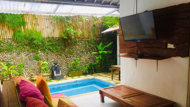 Área da piscina com parede de pedra, um banco de madeira e uma televisão na parede.