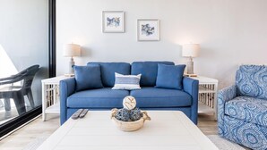 Una sala de estar moderna con un sofá azul, dos mesitas de noche con lámparas, una mesa de centro con objetos decorativos y obras de arte en la pared.