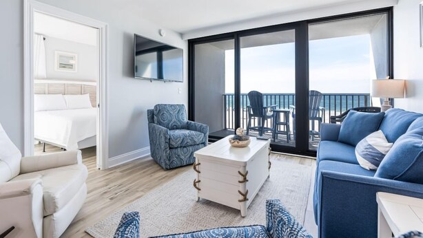 Una habitación de hotel moderna con balcón, sofá, sillón, mesa de centro y cama.