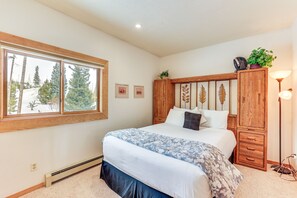 A bedroom with a large bed, wooden headboard, a window with a view of trees, and a floor lamp. - Mtn-View Gem w/ Community Perks in Silverthorne! (Silverthorne)