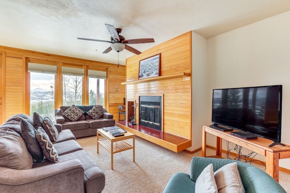 A modern living room with a fireplace, a television, and a large window offering a mountain view. - Mtn-View Gem w/ Community Perks in Silverthorne! (Silverthorne)
