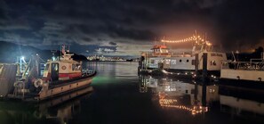 A nighttime harbor scene with boats docked, calm water, and a city skyline in the distance. - Luxury 2BR with Pool & Panoramic Golden Gate  and Skyline Views (Tiburon)