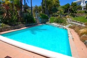 A rectangular swimming pool with clear blue water, surrounded by a stone border and a tiled deck.