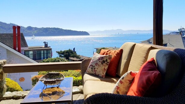 A balcony with a view of the sea, a sofa with cushions, and a small table with a decorative item.