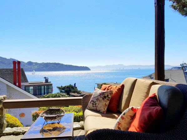 A balcony with a view of the sea, a sofa with cushions, and a small table with a decorative item.
