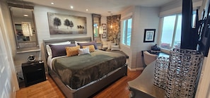 A modern bedroom with a large bed, a stone accent wall, and a view of the outdoors. - Luxury 2BR with Pool & Panoramic Golden Gate  and Skyline Views (Tiburon)