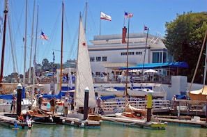 A marina with multiple boats docked, a building with a sign that reads 'Yacht Club', and people on the dock. - Luxury 2BR with Pool & Panoramic Golden Gate  and Skyline Views (Tiburon)