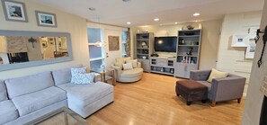 Ein Wohnzimmer mit einer Couch, Sesseln, einem Couchtisch und einer TV-Konsole mit einem Flachbildfernseher.