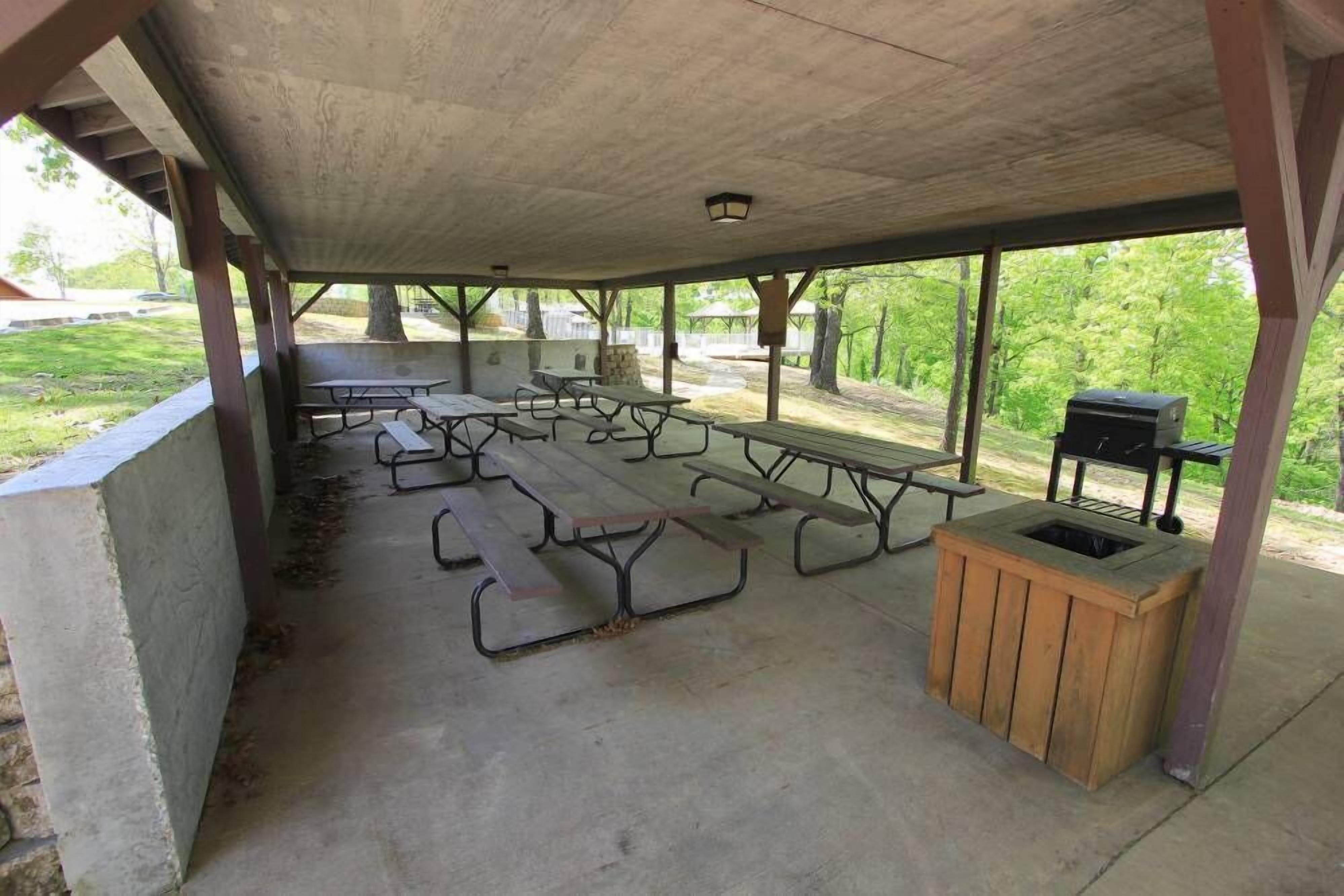 Un área de picnic techada al aire libre, con varias mesas y una parrilla.