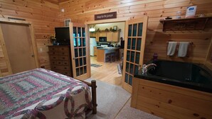 Interior de una cabaña de madera con una cama, un baño con bañera y una zona de cocina.