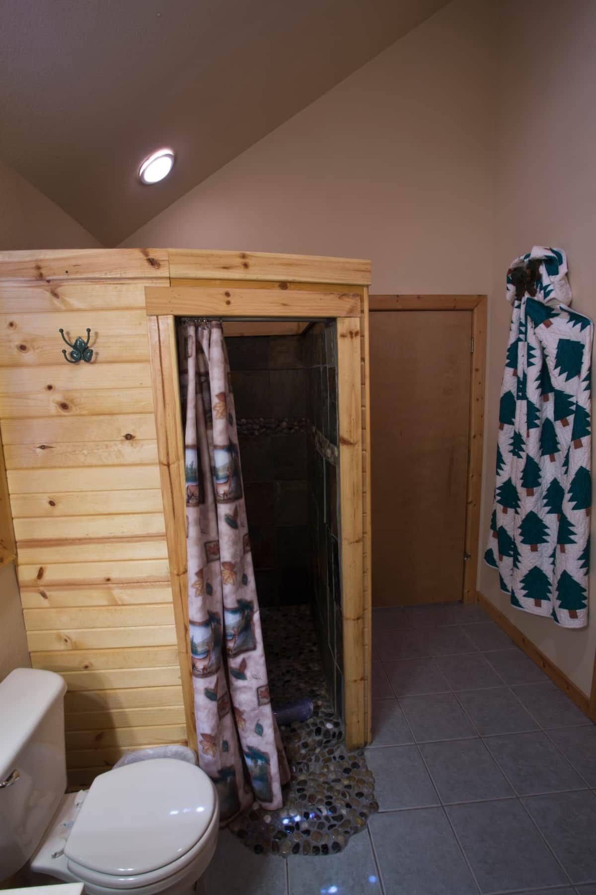 Een kleine houten badkamer met douche, toilet en douchegordijn.