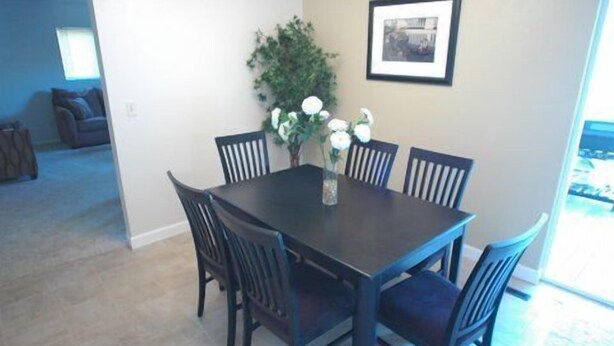 Un comedor con una mesa de madera oscura rodeada por seis sillas, un jarrón con flores blancas y un cuadro en la pared.