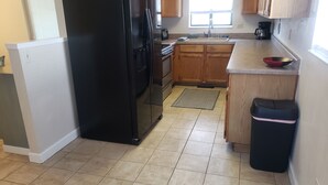 Una cocina con un refrigerador negro, armarios de madera, un lavamanos y una cafetera.