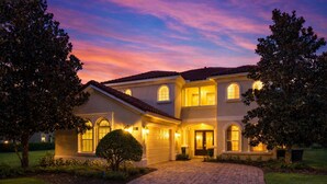 A two-story house with a brick driveway, arched windows, and a well-lit entrance. - Reunion Views | Movie Room, Amazing Views of the Tom Watson Golf Course (Kissimmee)