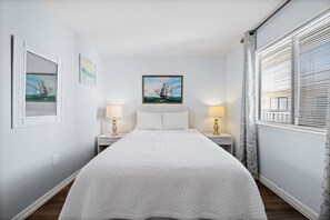 Quarto bem arrumado com uma cama grande, duas mesas de cabeceira com luminárias, um quadro emoldurado acima da cama e uma janela com persianas.