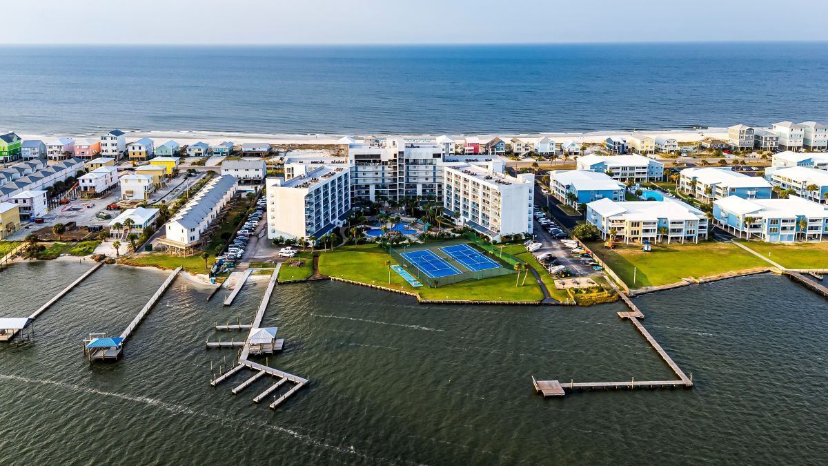 Vista aérea de un hotel costero con varias edificaciones, un puerto deportivo y una cancha de tenis.