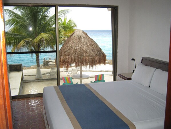 A hotel room with a large bed, a view of the beach, and a thatched umbrella.