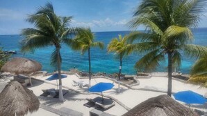 A beachside resort with thatched umbrellas, lounge chairs, and palm trees. - Small is Beautiful. Relax ON the beach, convenient & near the Presidential Villa (Cozumel)
