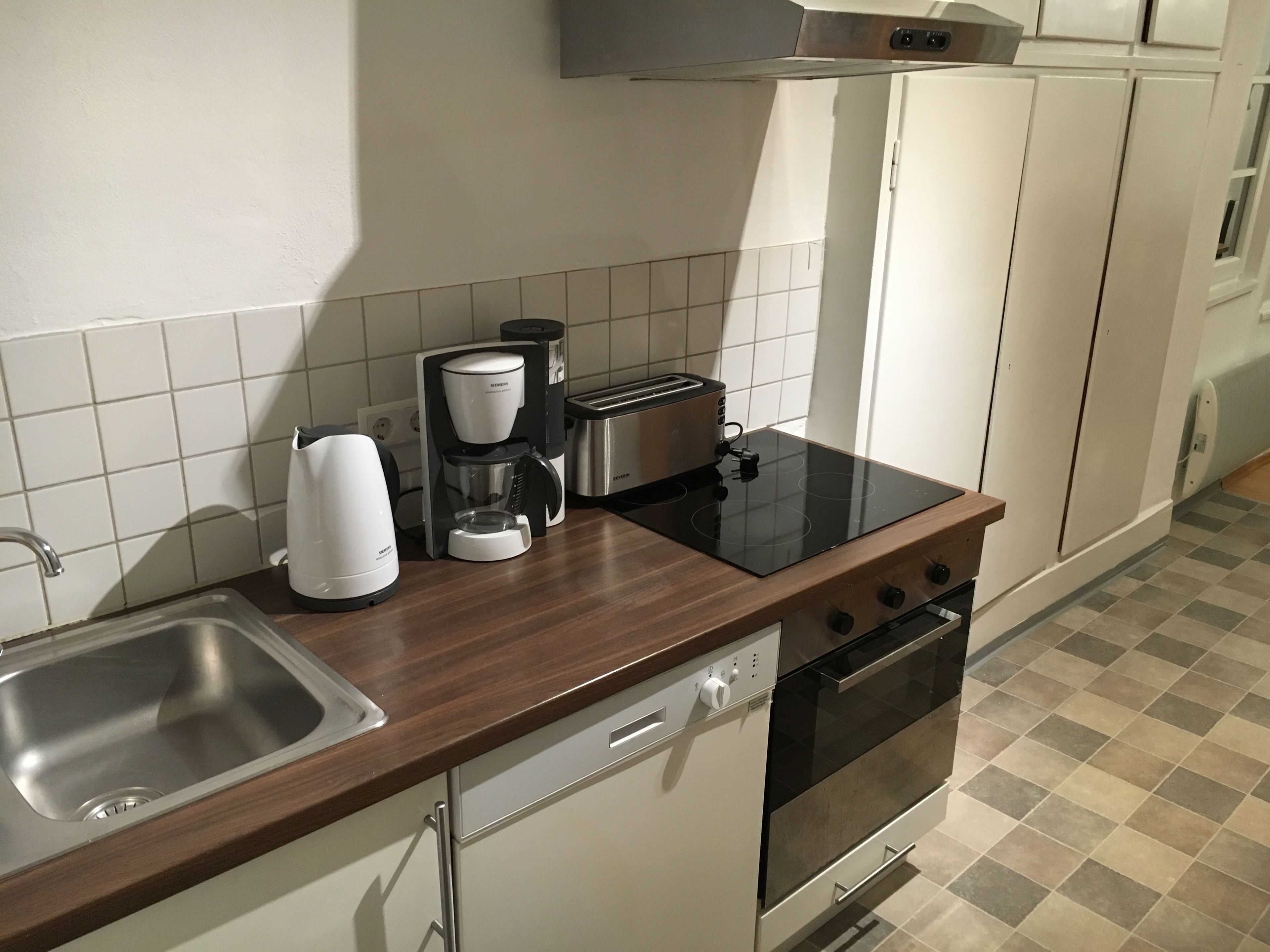 A modern kitchen with a stainless steel sink, a coffee maker, a toaster, and an oven.