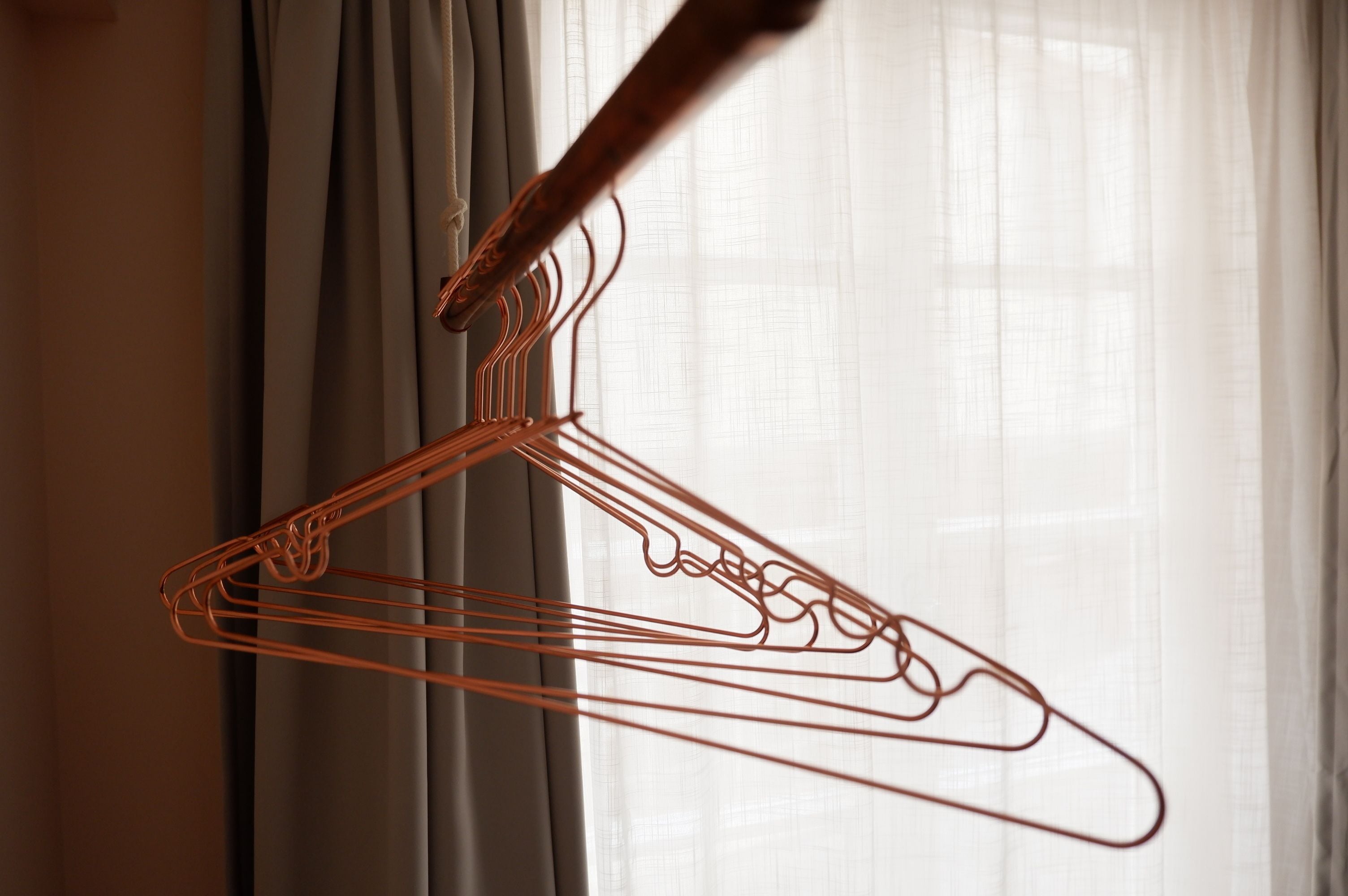 A wire hanger hanging against a window with sheer curtains.