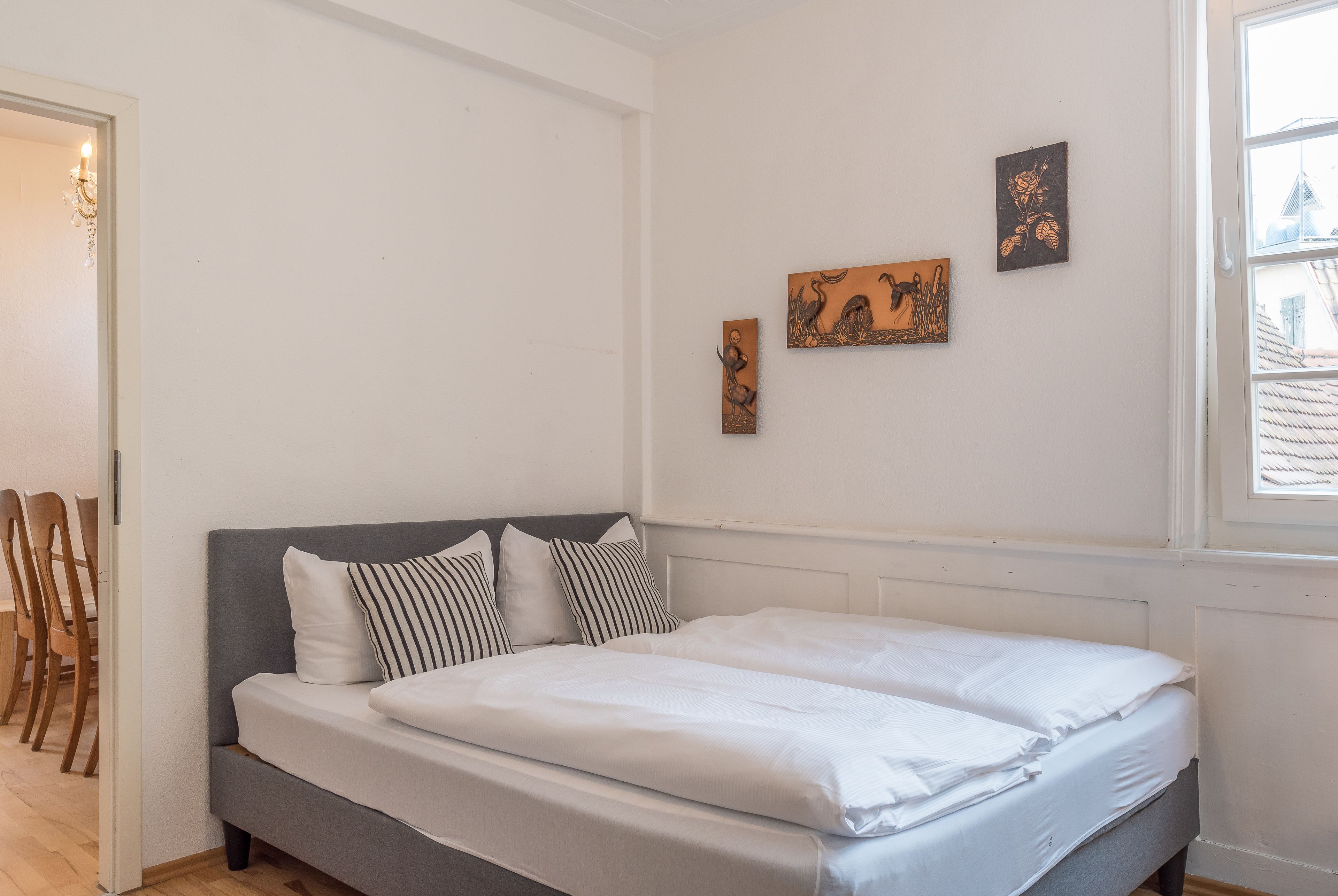 A bedroom with a double bed, a grey headboard, and three wall-mounted artworks.