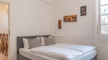 A bedroom with a double bed, a grey headboard, and three wall-mounted artworks.