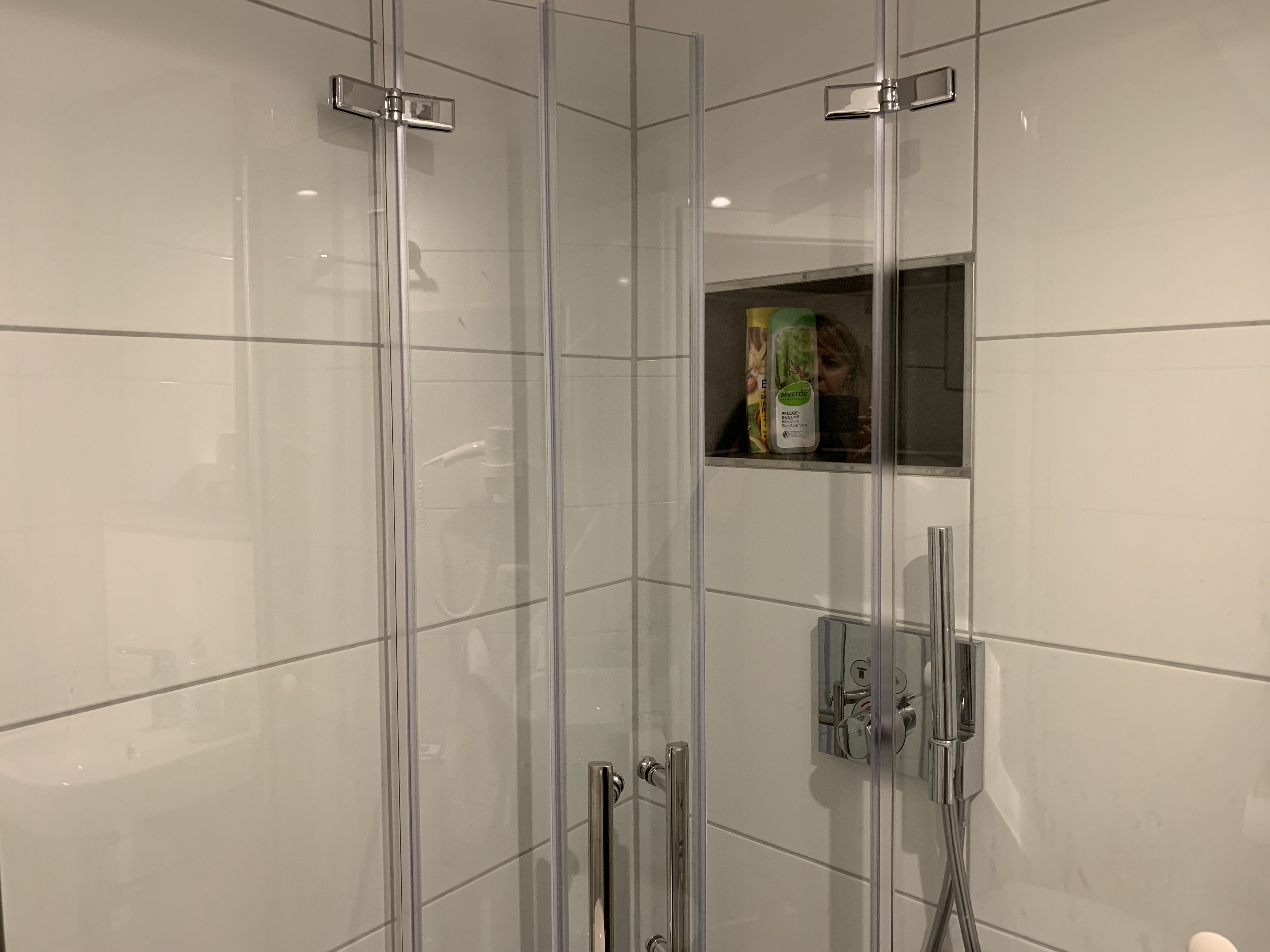 Een douchecabine met glazen wanden, een handdouche en een bedieningspaneel aan de muur.