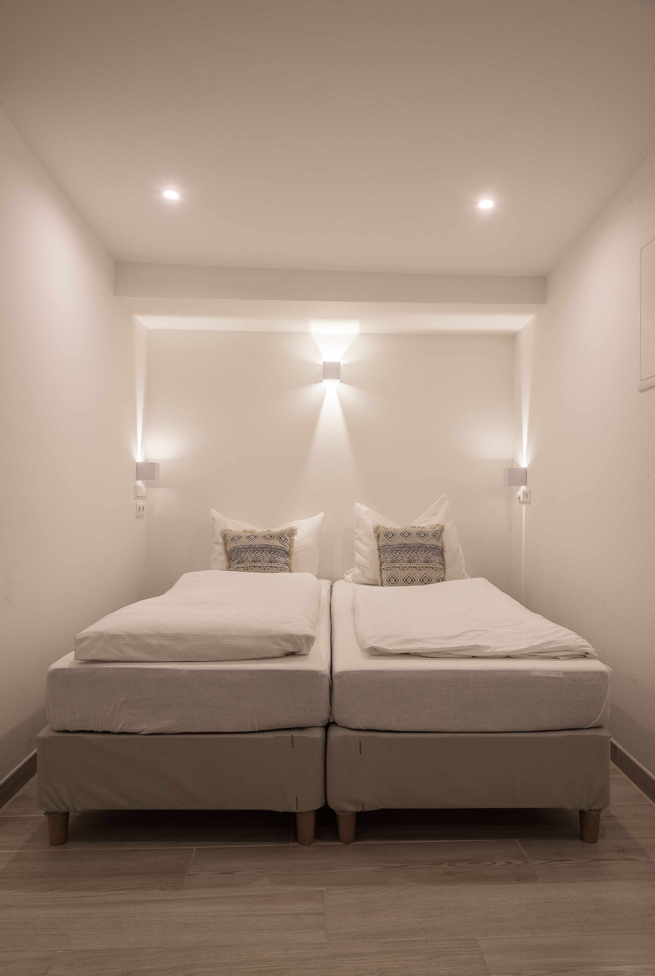 A twin room with two beds, a small bedside table, and a wall-mounted light fixture.