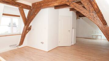 Habitación en ático con vigas de madera a la vista, una puerta blanca y vistas al exterior a través de una ventana.