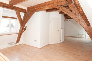 Habitación en ático con vigas de madera a la vista, una puerta blanca y vistas al exterior a través de una ventana.