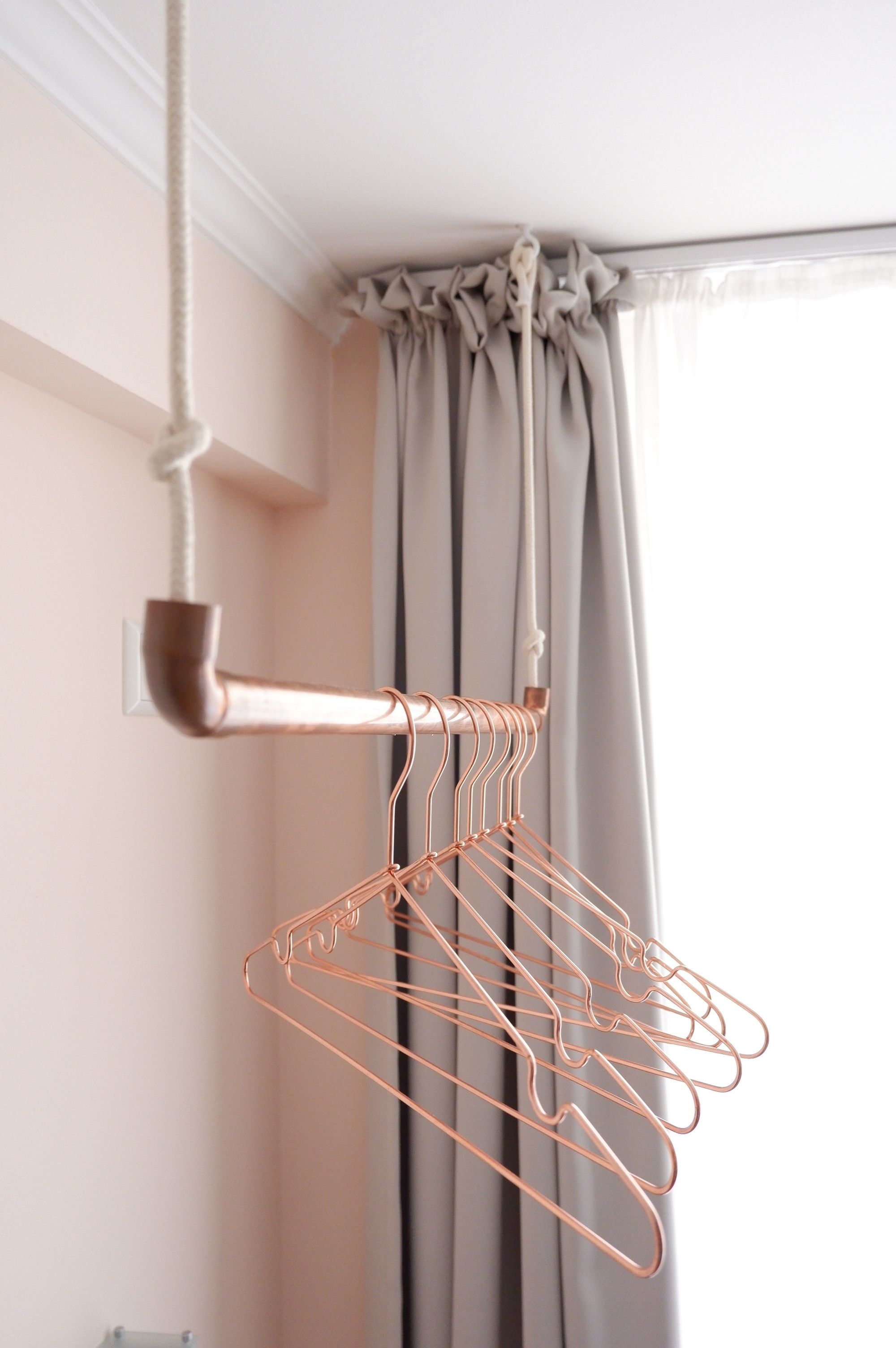 A copper wire coat rack in a room with a window and curtains.