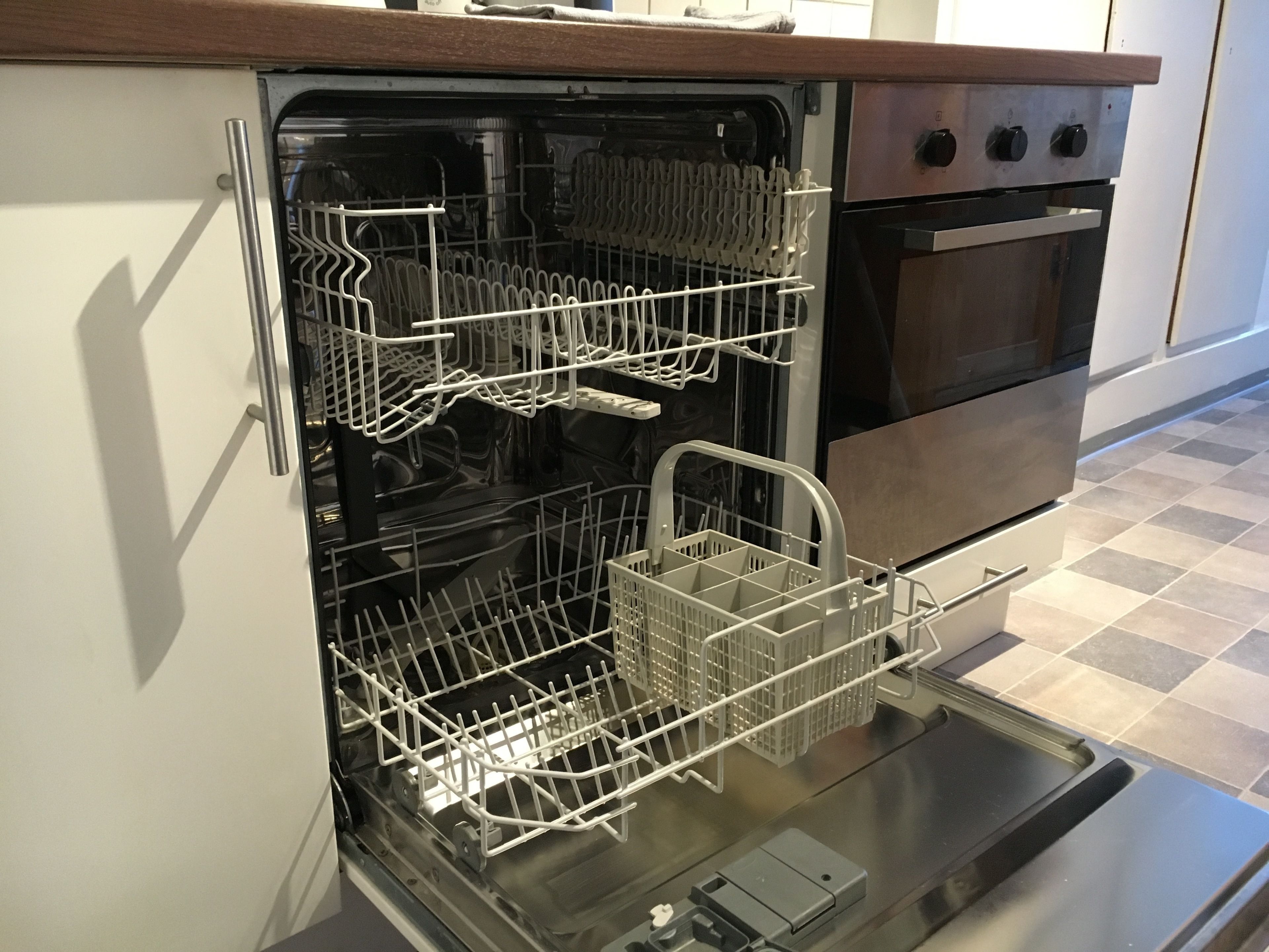 An open dishwasher with multiple racks and a silver oven in the background.