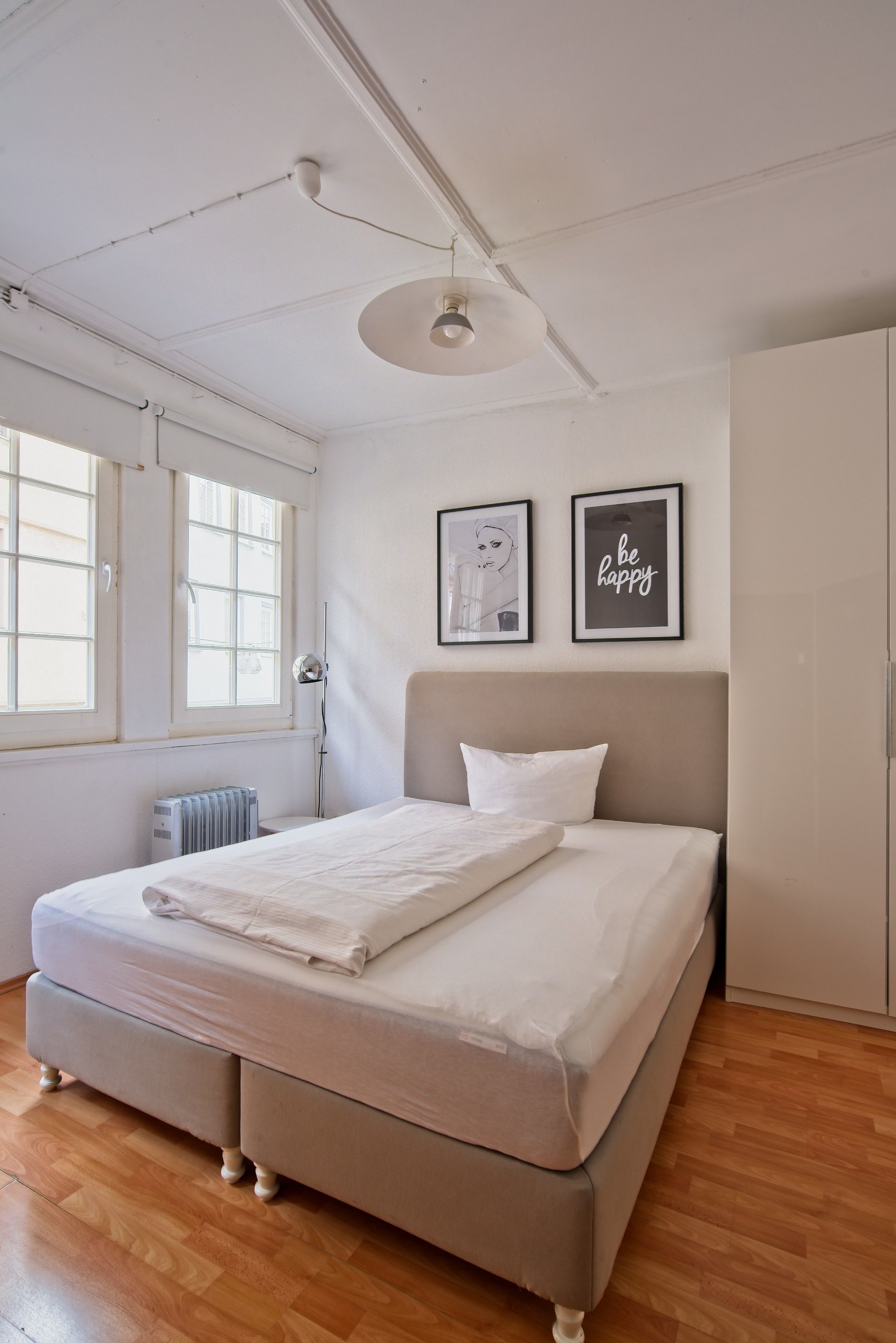 Una camera da letto con un letto, un termosifone, una finestra e due quadri appesi al muro.
