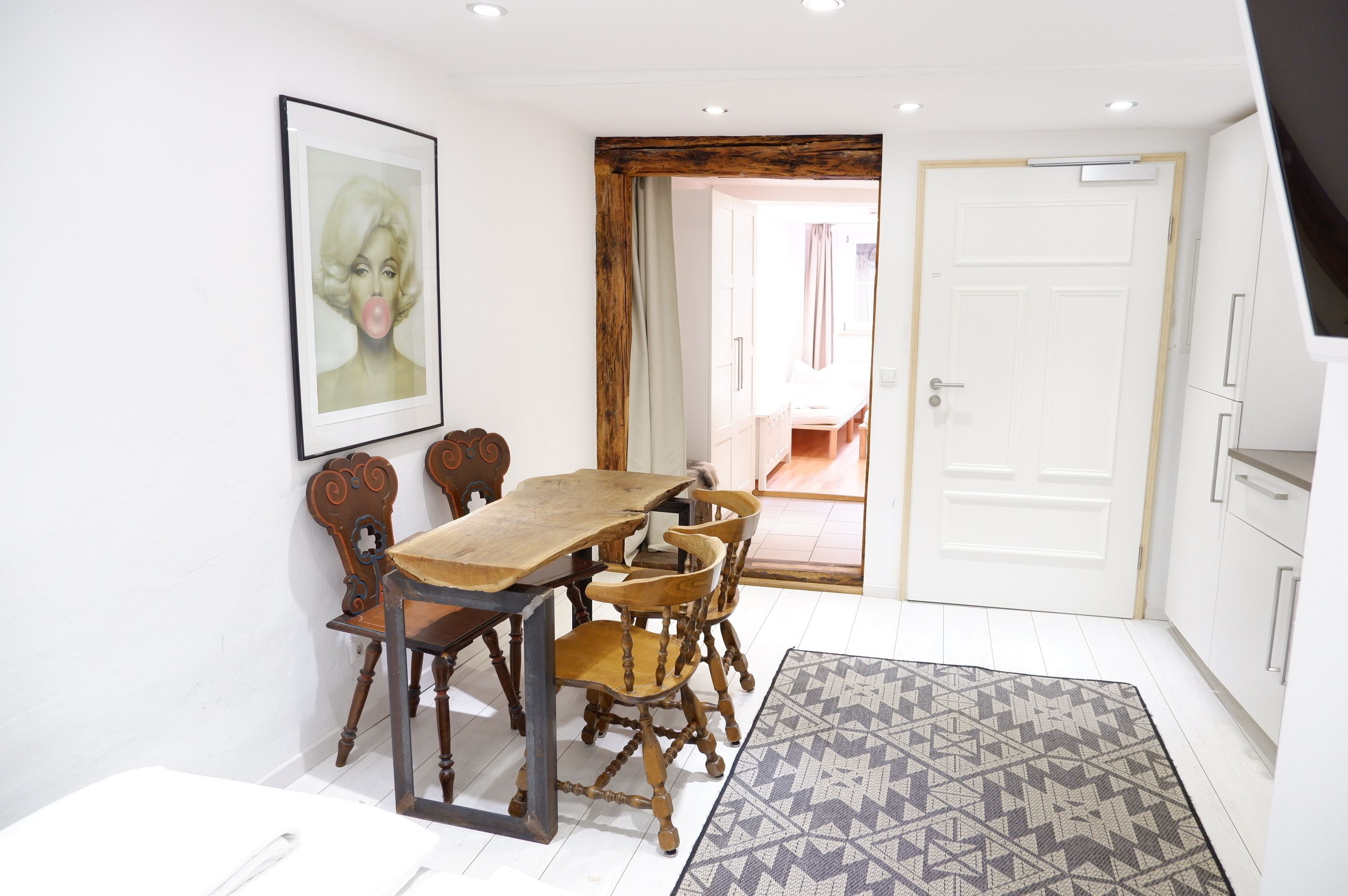 Un coin repas avec une table et des chaises en bois, un tableau encadré au mur et un tapis à motifs sur le sol.