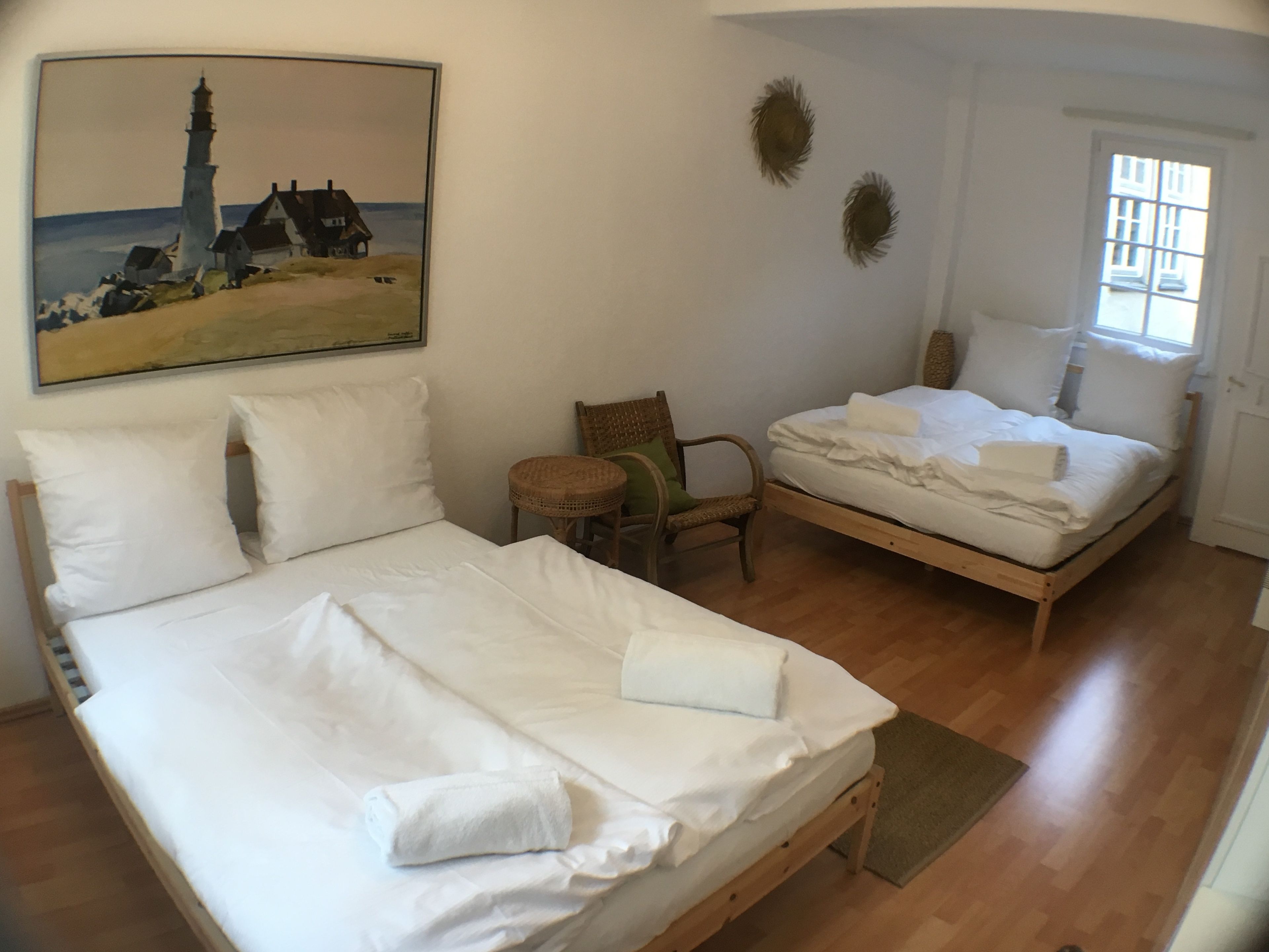 Una stanza con due letti, una sedia, un tavolino e un quadro raffigurante un faro.