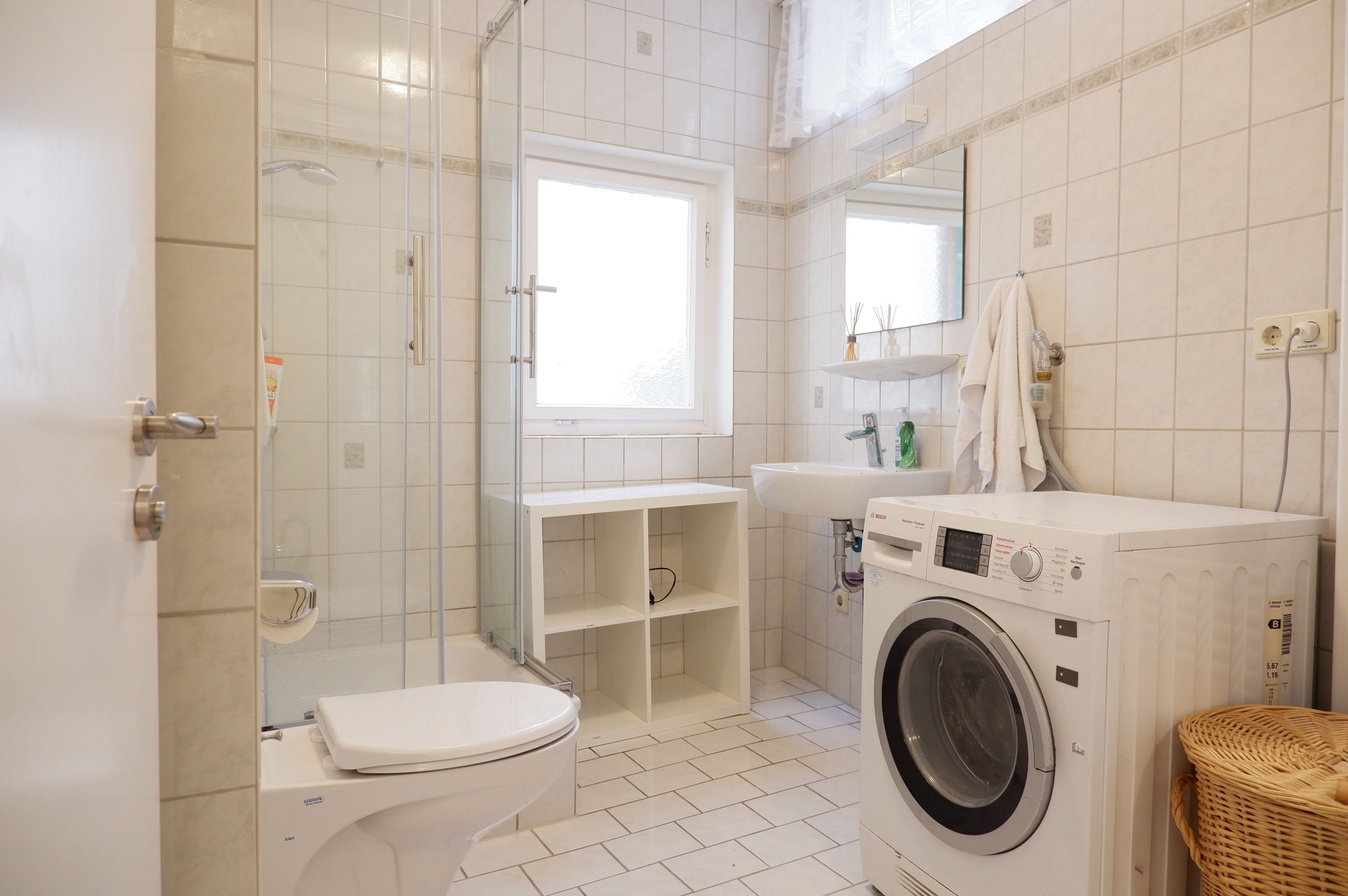 A compact bathroom with a toilet, a washing machine, a sink, and a shower area.