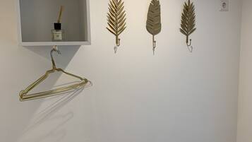 A wall with a white shelf holding a bottle of reed diffuser and four wall-mounted hooks with decorative items.
