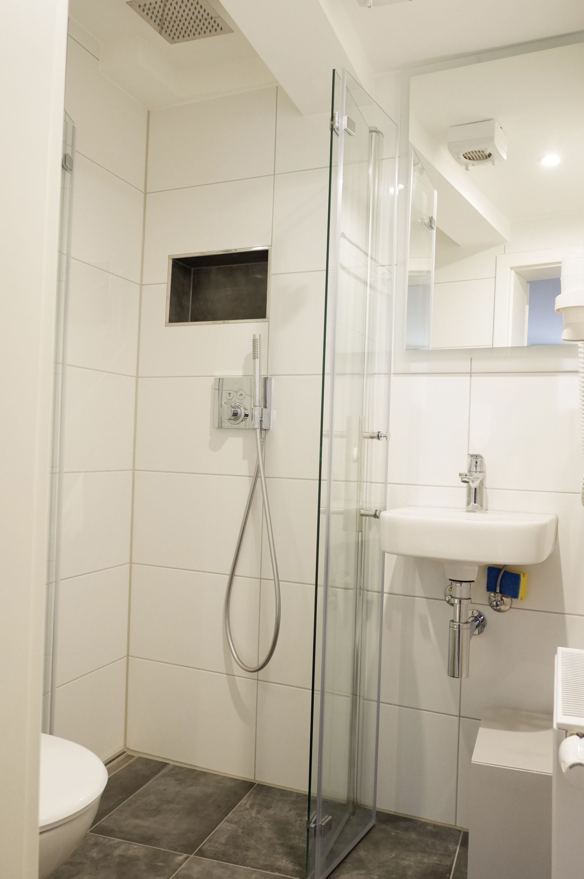 Un baño moderno con cabina de ducha de vidrio, un lavabo blanco y un inodoro.